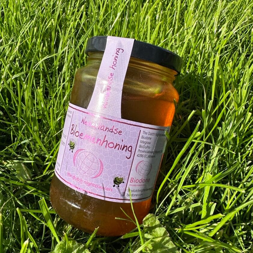 Pot Nederlandse bloemenhoning in het gras, met een natuurlijke en rustieke uitstraling.