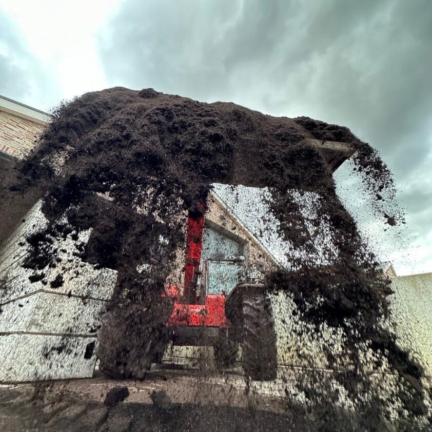 Wormcompost losgestort door een rode telescooplader.